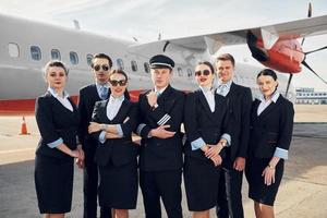 posando para uma câmera. tripulação de trabalhadores do aeroporto e avião em roupas formais juntos ao ar livre foto