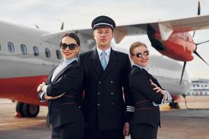 posando para uma câmera. tripulação de trabalhadores do aeroporto e avião em roupas formais juntos ao ar livre foto