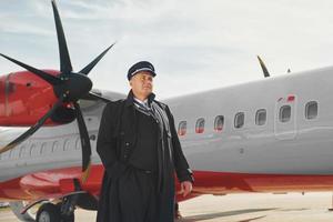 olhando para longe. piloto em uniforme preto formal está ao ar livre perto de avião foto