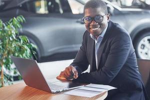 trabalhador de escritório está sentado em autosalon por mesa com laptop foto