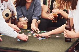 jogando e sentado à mesa. grupo de jovens em roupas casuais faz uma festa no telhado juntos durante o dia foto