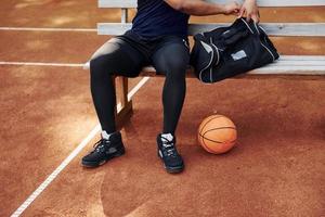 senta-se com bolsa preta e se preparando para o jogo. homem afro-americano joga basquete na quadra ao ar livre foto