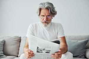 senta no sofá. homem moderno elegante sênior com cabelos grisalhos e barba dentro de casa foto