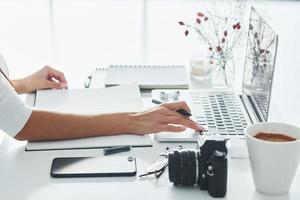 usando laptop e bloco de notas. jovem freelancer trabalhando dentro de casa no escritório durante o dia foto