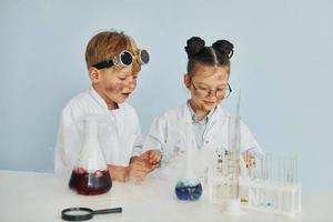 menino trabalha com líquido em tubos de ensaio. crianças em jalecos brancos interpretam cientistas em laboratório usando equipamentos foto