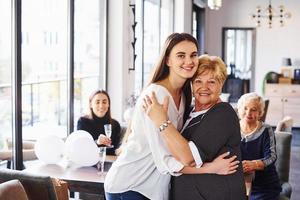 abraçando um ao outro. mulher sênior com família e amigos comemorando um aniversário dentro de casa foto