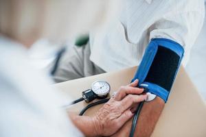vista de perto. médica usa tonômetro para fazer medição de pressão arterial para homem sênior foto