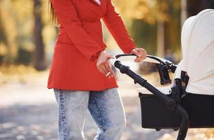 vista de perto. mãe de casaco vermelho dá um passeio com seu filho no carrinho no parque no outono foto