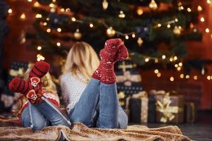 mãe com sua filhinha deitada no chão dentro de casa em roupas festivas nas férias de natal foto