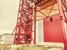 local de construção. torneira alta, metálica e vermelha ao lado do armazém. portão de metal, entrada da fábrica foto