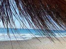 vista do mar azul com água salgada através da palha seca amarela do guarda-sol na praia no resort paraíso do sul do país tropical oriental quente. o fundo foto