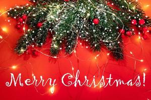 cartão festivo de natal com ramos de abeto, neve, bagas vermelhas, luzes de natal em vermelho com a legenda feliz natal. foto