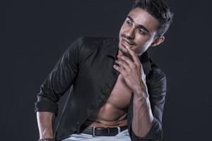 belo modelo masculino árabe com corpo perfeito posando no estúdio. retrato de um modelo masculino atlético posando em fundo escuro no estúdio. conceito de moda. foto