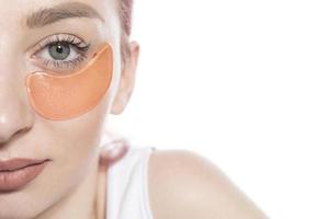 mulher bonita com manchas cosméticas hidratando a pele sob os olhos. isolado no fundo branco foto