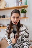 mulher engraçada cantando na espátula, segurando a espátula como microfone. foto