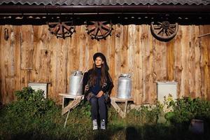 mulher senta-se em um banco com latas de leite em uma fazenda foto