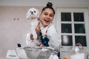 mulher sorridente na cozinha segurando cachorro maltês branco fofo foto