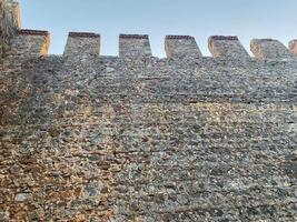 grande parede de pedra de uma antiga fortaleza medieval feita de paralelepípedos contra um céu azul foto