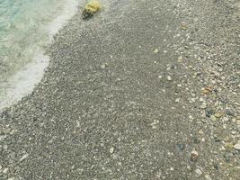 férias à beira-mar na praia. praia de seixos com pedras. na praia encontra-se uma pedra amarela, que é lavada pelas ondas brancas do mar com espuma foto