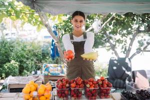 jovem vendedora segurando pimentão e tomate nas mãos foto