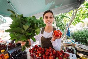 jovem vendedora no trabalho, segurando salsa e tomate nas mãos foto