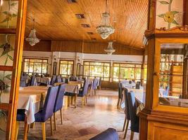 salão espaçoso com mesas e cadeiras. sala de jantar no hotel para as refeições. turistas no almoço. candelabros de cristal caros pendurados no teto de madeira foto