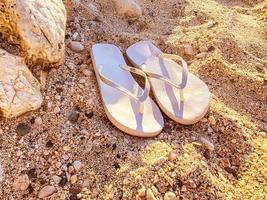 chinelos de borracha branca ficam na areia. sapatos do mar. ardósias para caminhar ao longo da costa do mar. chinelos femininos que são usados em um dedo foto