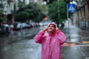 jovem sorridente com capa de chuva enquanto desfruta de um dia chuvoso. foto