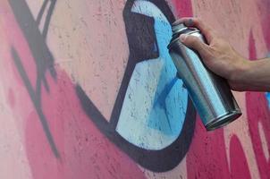 uma mão com uma lata de spray que desenha um novo grafite na parede. foto do processo de desenho de um grafite em um close-up da parede de madeira. o conceito de arte de rua e vandalismo ilegal