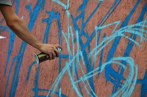 uma mão com uma lata de spray que desenha um novo grafite na parede. foto do processo de desenho de um grafite em um close-up da parede de madeira. o conceito de arte de rua e vandalismo ilegal