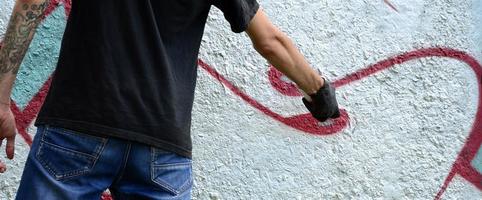 um jovem hooligan pinta graffiti em uma parede de concreto. conceito de vandalismo ilegal. arte de rua foto