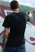 um jovem hooligan pinta graffiti em uma parede de concreto. conceito de vandalismo ilegal. arte de rua foto