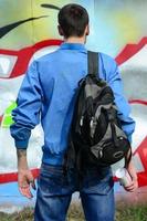 um jovem grafiteiro com uma bolsa preta olha para a parede com seu grafite na parede. conceito de arte de rua foto