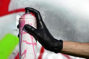 uma mão com uma lata de spray que desenha um novo grafite na parede. foto do processo de desenho de um grafite em uma parede de metal. o conceito de arte de rua e vandalismo ilegal