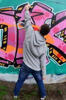 um jovem com um capuz cinza pinta graffiti em rosa e verde c foto