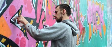 um jovem com um capuz cinza pinta graffiti em rosa e verde c foto