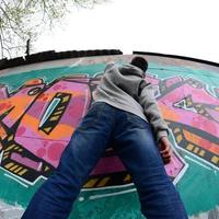 um jovem com um capuz cinza pinta graffiti em rosa e verde c foto