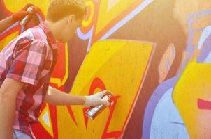 um jovem grafiteiro ruivo pinta um novo graffiti na parede. foto do processo de desenho de um grafite em um close-up da parede. o conceito de arte de rua e vandalismo ilegal