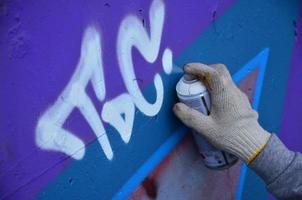 uma mão com uma lata de spray que desenha um novo grafite na parede. foto do processo de desenho de um grafite em um close-up da parede de concreto. o conceito de arte de rua e vandalismo ilegal