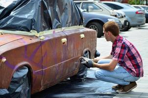 um jovem grafiteiro ruivo pinta um novo grafite colorido no carro. foto do processo de desenho de um grafite em um carro close-up. o conceito de arte de rua e vandalismo ilegal