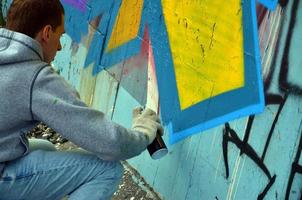 um jovem grafiteiro ruivo pinta um novo graffiti na parede. foto do processo de desenho de um grafite em um close-up da parede. o conceito de arte de rua e vandalismo ilegal