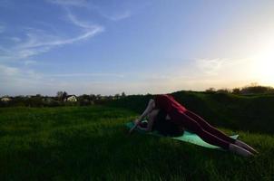 duas jovens loiras em trajes esportivos praticam ioga em uma pitoresca colina verde ao ar livre à noite. o conceito de esporte exercitando ao ar livre foto