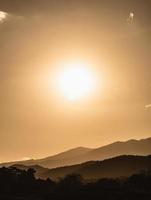 paisagem por do sol com iluminação de ouro de montanha e sol sob o céu de noite colorido vibrante nas montanhas. natureza montanha céu e nuvens conceito de pôr do sol foto