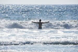 homem sem camisa despreocupado com os braços estendidos em pé no meio do mar foto