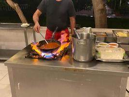 chef, cozinhe cozinhando em uma frigideira no fogo comida em um restaurante em uma cozinha aberta em um hotel com tudo incluído em um resort turístico paradisíaco tropical quente de férias foto