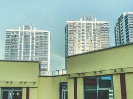 arco-íris em uma área residencial moderna. casas de vidro altas e de vários andares perto do shopping center. arco-íris no céu depois da chuva foto