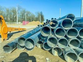 tubos para a construção de comunicações no novo microdistrito. tubos de plástico preto na areia e detritos. equipamento de construção amarelo ao lado dos canos foto