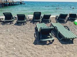 férias à beira-mar na praia. no solo de seixos existem espreguiçadeiras para os turistas se bronzearem. há colchões e tecido verde nas espreguiçadeiras. as pessoas nadam fundo foto