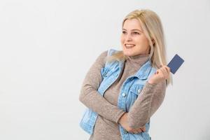 retrato de uma linda jovem loira de suéter mostrando cartão de crédito e desviando o olhar para o espaço da cópia isolado fundo branco foto