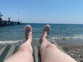 pernas peludas masculinas de um turista em uma espreguiçadeira na praia à beira-mar foto